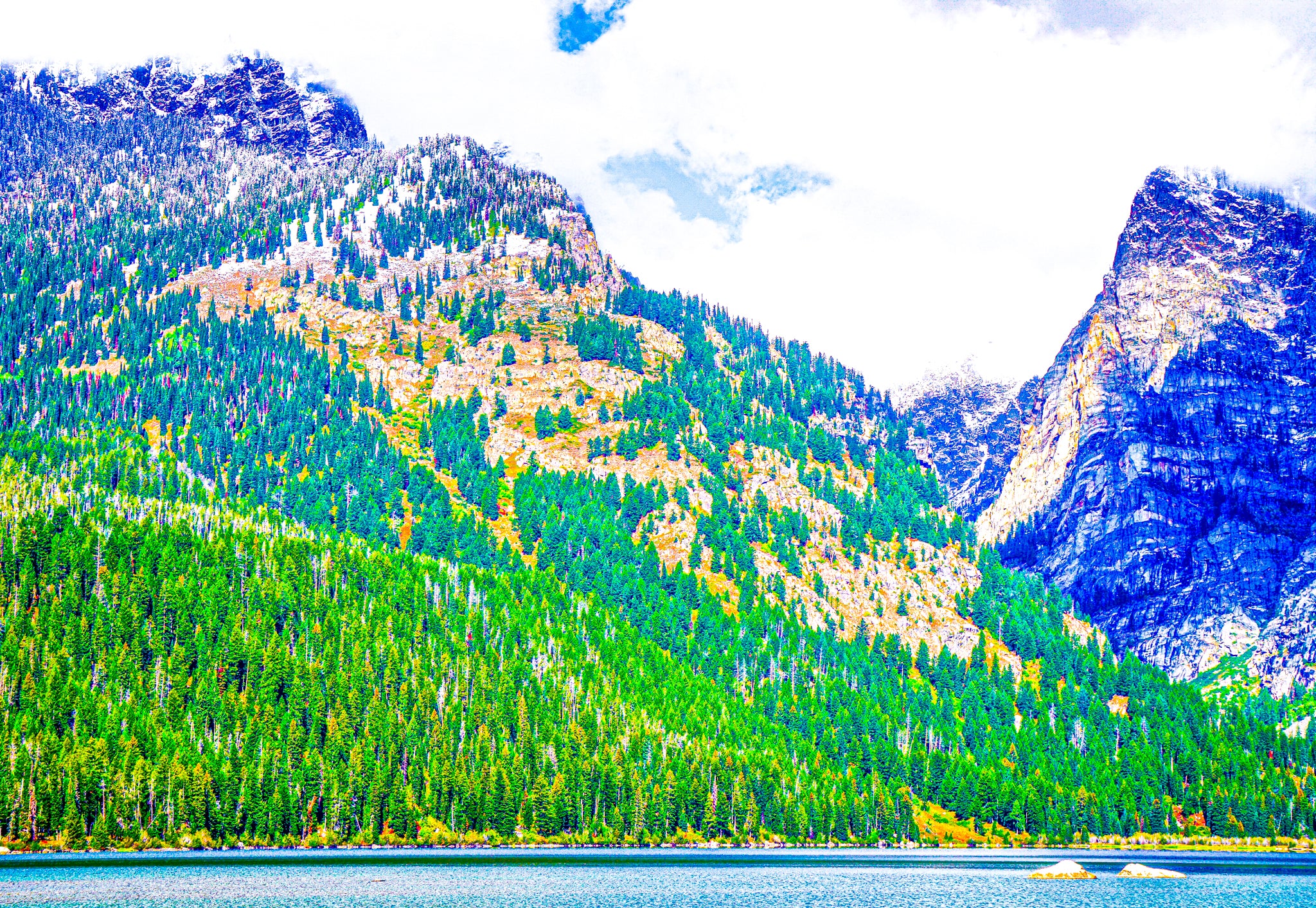Two big rocks and two small rocks make for an interesting composition in this photograph along with the narrow strip of water in the foreground. These Tetons are like skyscrapers of their own, reaching into the clouds of the stratosphere.